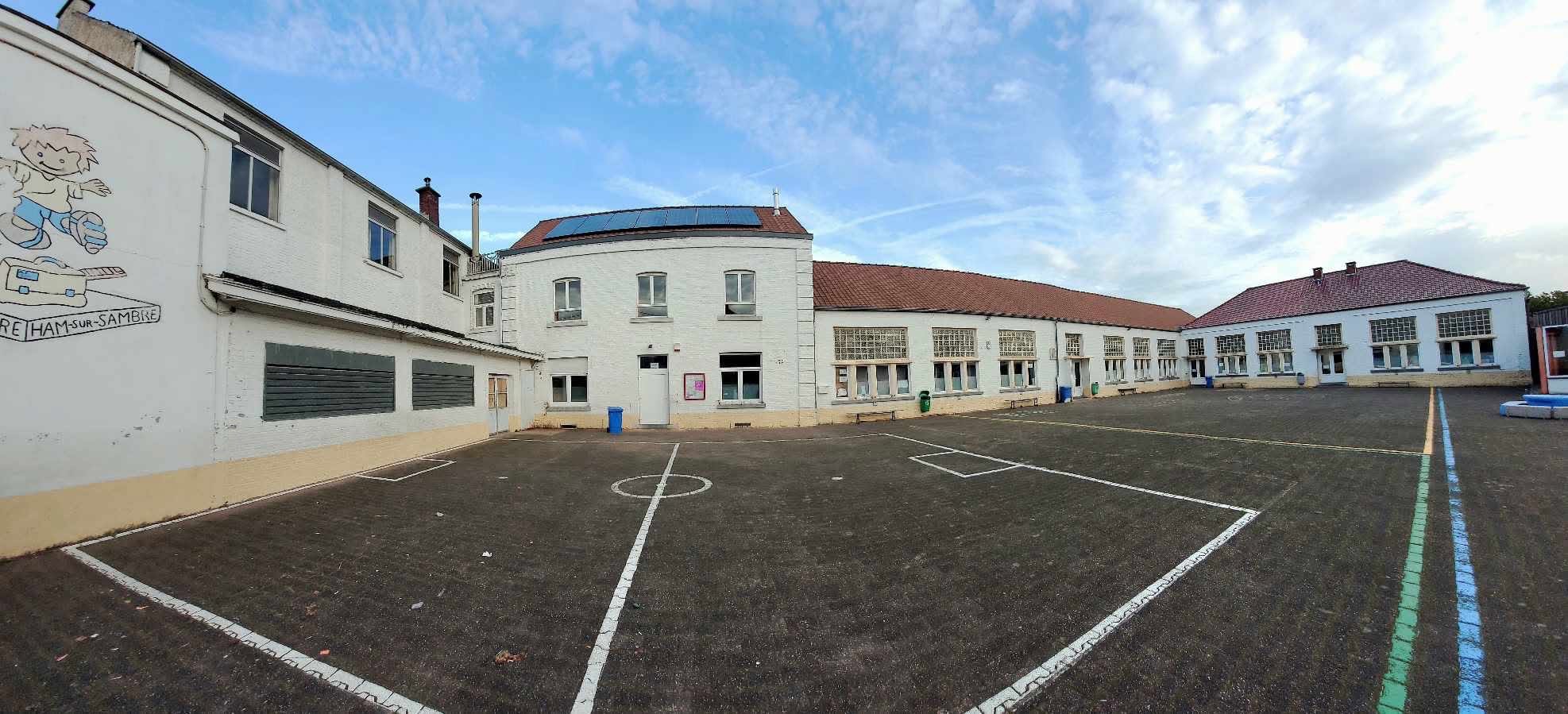 La grande cour de récréation et les bâtiments de l’école, avec la fresque du petit Victor